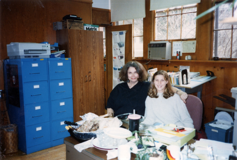 Two women sitting at a table in the Women's Center. There's a carved turkey and a pile of dishes in front of them.