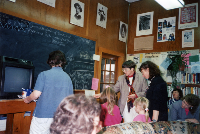 Judy Wallins, the woman with the scarf, pointing at something in the Women's Center. There are several other people in the shot, but most have their faces turned away from the camera.