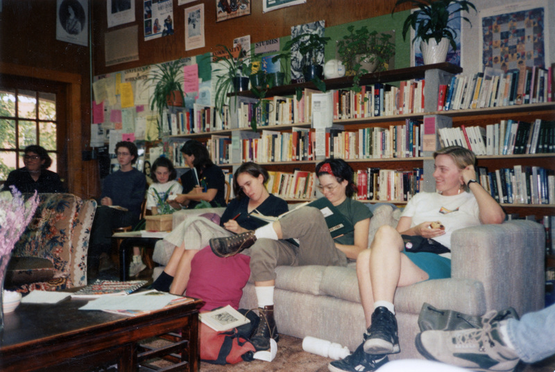 A group of people attending the Women's Center Open House. One appears to be writing notes, another is flipping through a book, and a third is holding something in their hand. There are more people in the background of the shot.