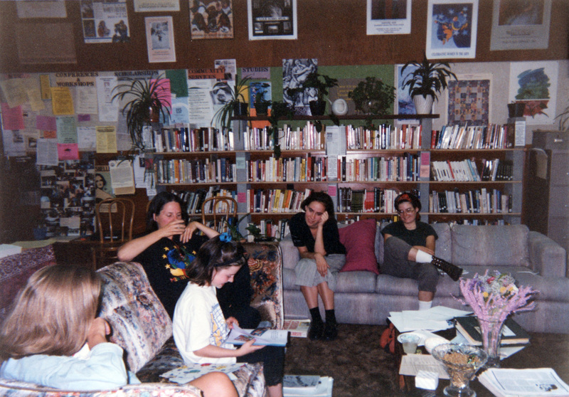 A group of people sitting in the Women's Center. A child is reading a book while the adults nearby listen to her.