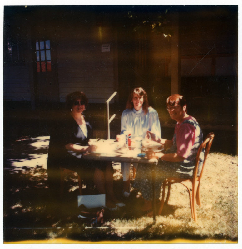 Left to Right: Dianne Milhollen, an unidentified woman, and Betsy Thomas sitting at a table outside the Women's Center.
