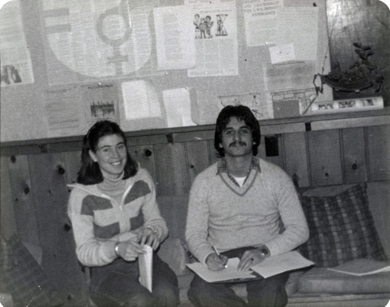 Two people sitting in the Women's Center. One appears to be writing something. Both are smiling at the camera.