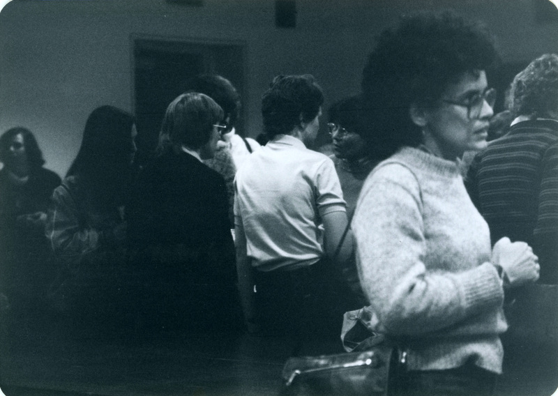 Ruth Windhover, a UI English Professor, stands to the far right in the foreground of a crowd shot. Marilyn Francis and Kay Keskinen are standing behind people wearing white. 