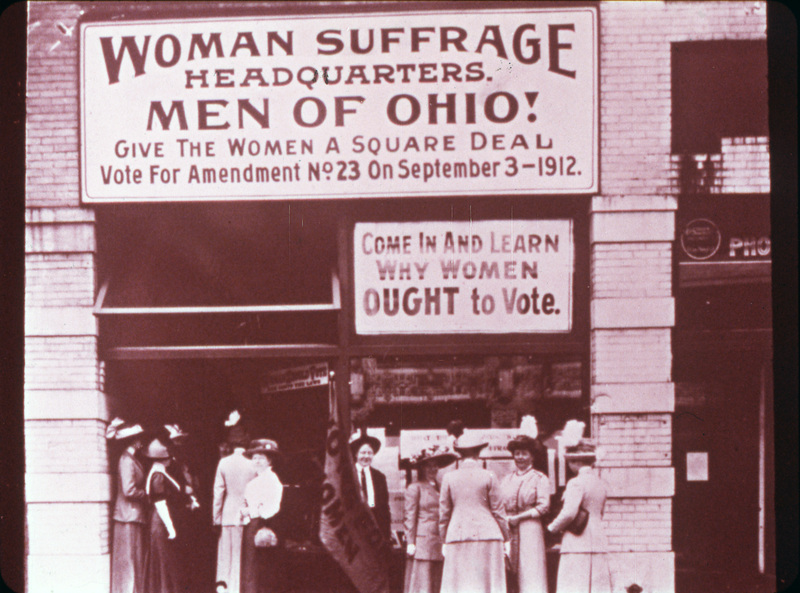 A group of women standing outside Woman Suffrage Headquarters in Upper Euclid Avenue, Cleveland. One sign reads "Woman Suffrage Headquarters. Men of Ohio! Give the women a square deal. Vote for Amendment No. 23 on September 3, 1912." Another reads "Come in and learn why women ought to vote." Courtesy Library of Congress.
