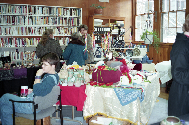 Several women sitting and standing during an early Womens Work Arts and Crafts Fair in the Women's Center in the old Journalism building on the corner of Line Street and Idaho Avenue. Amy Wilson (wearing a brown plaid shirt) talks to two unidentified women in the background. Gwen Snow is seated in the foreground. The event was started by Rebecca Rod, a local potter and later the U of I's first LGBTQ Program Coordinator.