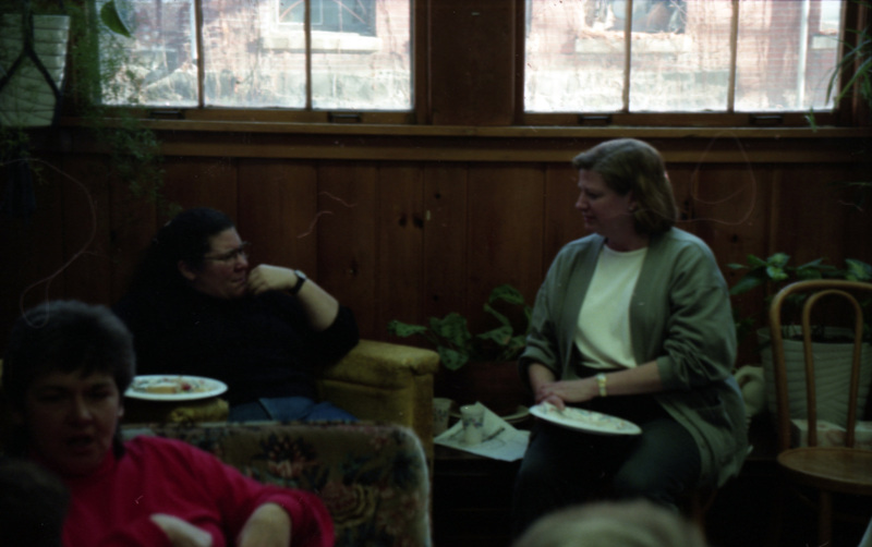 Jill Anderson and unidentified woman talking in the Women's Center. They sit on chairs in front of a wall with windows. Another woman wearing pink sits in the foreground.