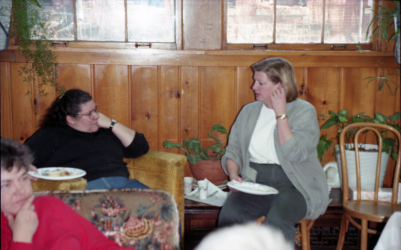 Jill Anderson (furthest right) and an unidentified woman talking in the Women's Center. They sit on chairs in front of a wall with windows. Another woman wearing pink sits in the foreground.