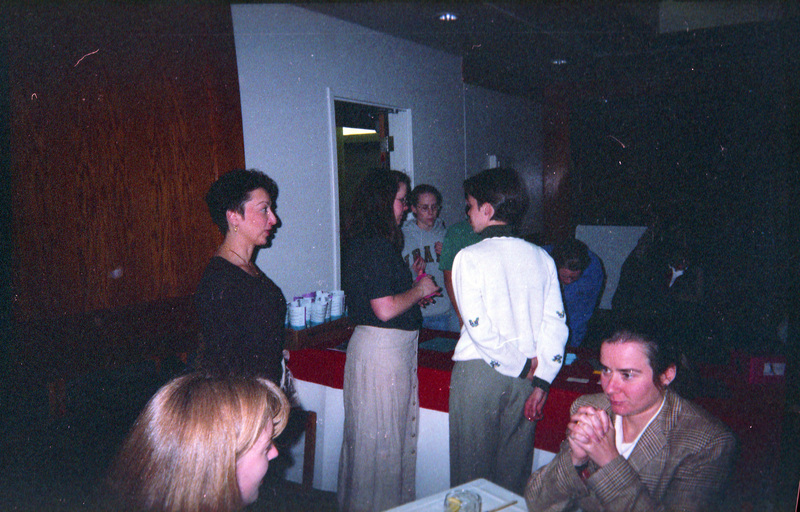 People milling about at an event. Some people are standing and talking, others are seated. Valerie Russo can be seen standing on the left, her profile in view. The woman in the white sweater is Mary Lu Schweitzer.
