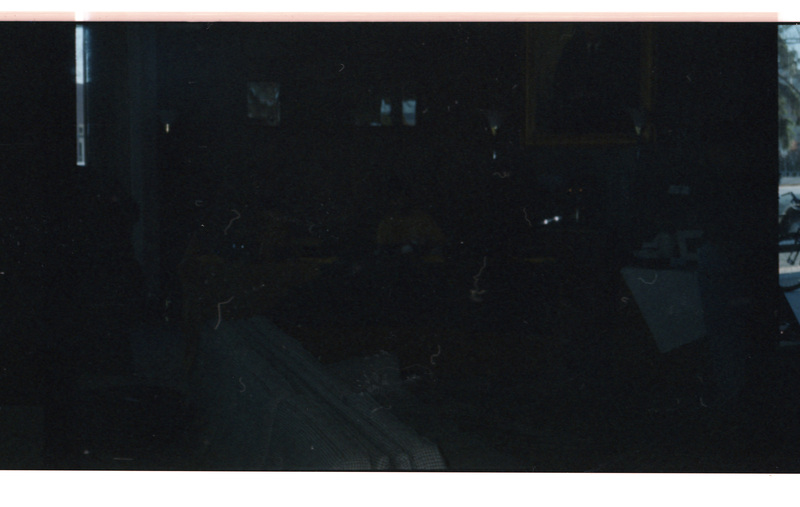 A dimly lit photo. There appears to be a person sitting near couches and a wall with a large portrait painting.