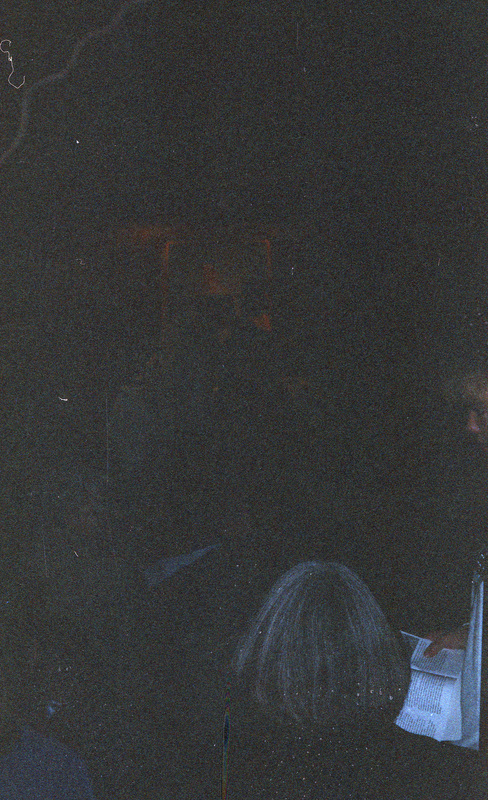 A dimly lit photo. There appears to be a painted portrait in the background and people sitting before it.
