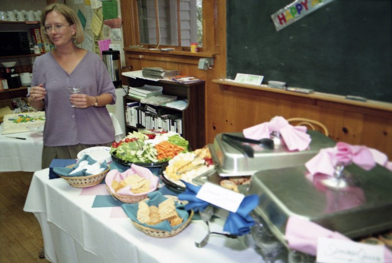 Susan Palmer grabbing food from a buffet spread. She wears a purple shirt and holds a glass.