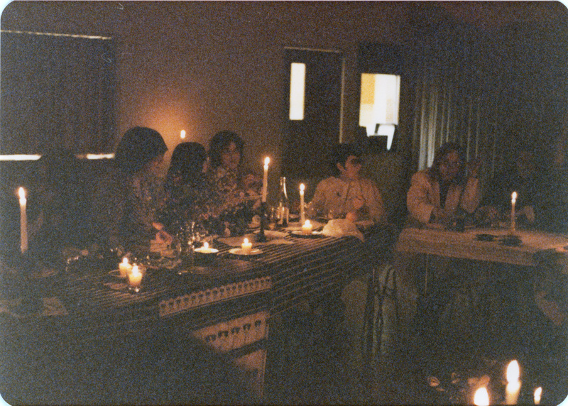 Photo from a recreation of Judy Chicago's The Dinner Party, held in St. Augie's. Several people sitting at tables. The room is lit by candlelight.