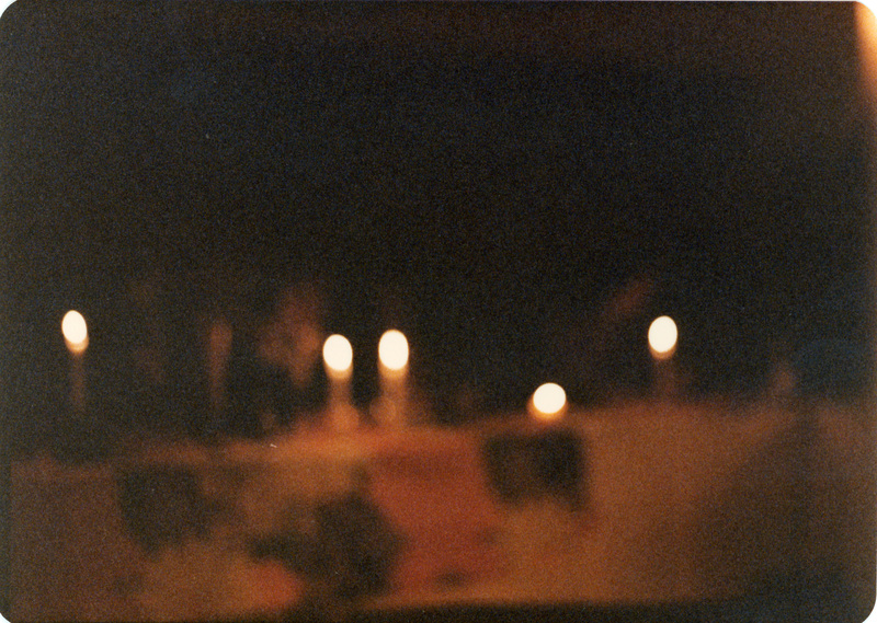 Photo from a recreation of Judy Chicago's The Dinner Party, held in St. Augie's. A blurry photograph of people sitting behind a candlelit table.