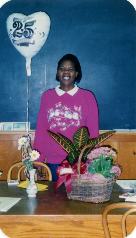 A woman standing next to a 25th anniversary balloon and a basket of flowers.