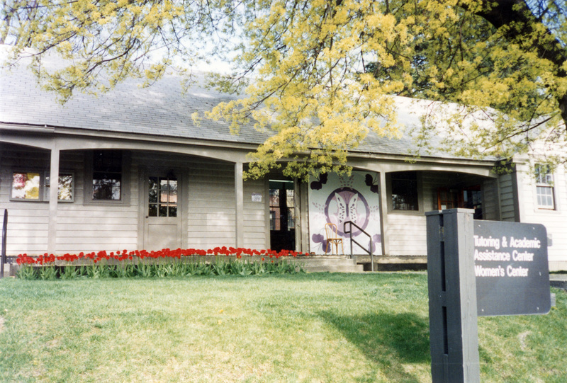A shot of the outside of the Tutoring and Academic Assistance Center and Women's Center. A row of red tulips line the front of the building. A signpost can be seen in the bottom right of the image.