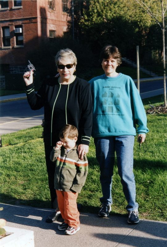 A woman (left) holds a race gun while Jeannie Harvey (in green) holds a stopwatch. Both are looking at the camera. A small child stands in front of them.