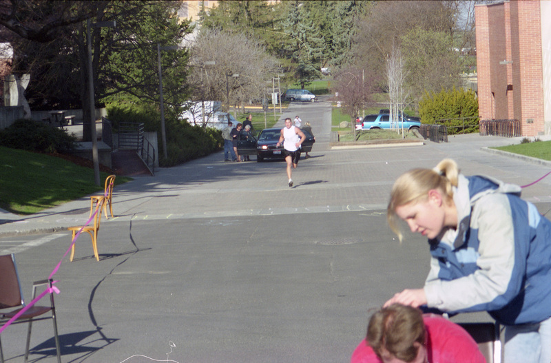 A man running towards the finish line. People are getting into a car behind him.
