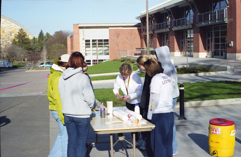 A group of people, including Jill Anderson, at a table at the Fun Run finish line. Jill Anderson is bending over the table wearing a yellow lanyard.