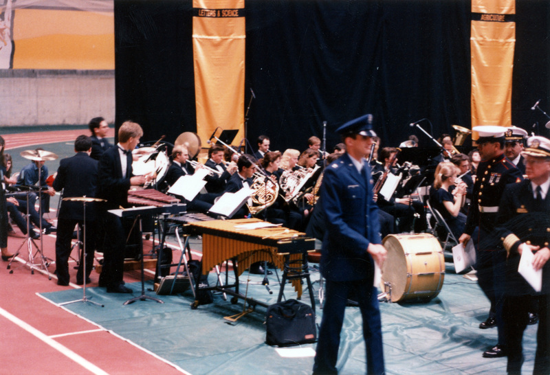 A shot of people in military uniforms walking by a musical ensemble.