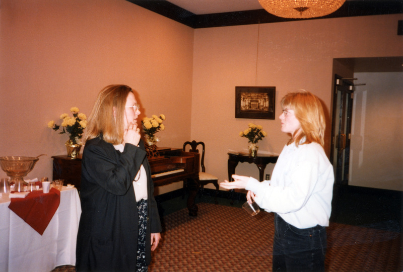 Susan Palmer (left) talks to another woman, both wearing relatively fancy clothing. They appear to be in the lobby for the Administration Auditorium.