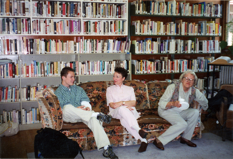 From left to right: unidentified man, Valerie Russo, and Isabel Miller, sitting on a couch in the Women's Center. Two large bookshelves cover the wall in the background.