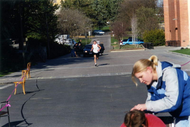 A man running towards the finish line. People are getting into a car behind him.