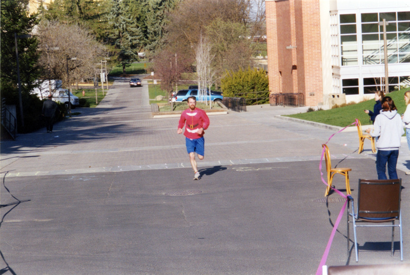 A man wearing a santa shirt running towards the finish line.