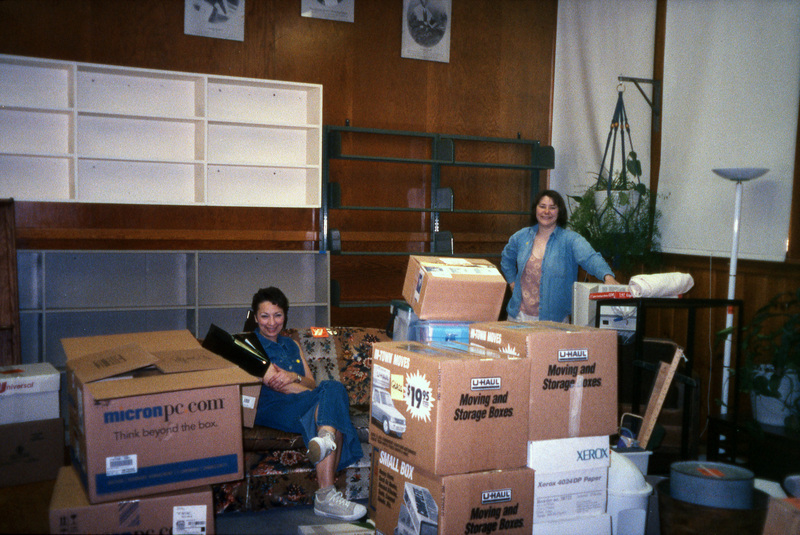 Valerie Russo (left) and an Chaucey Wittinger (right) smiling at the camera amid piles of moving boxes. Women's Center relocation from the Old Journalism Building to the Theatre Annex, Summer 2000.