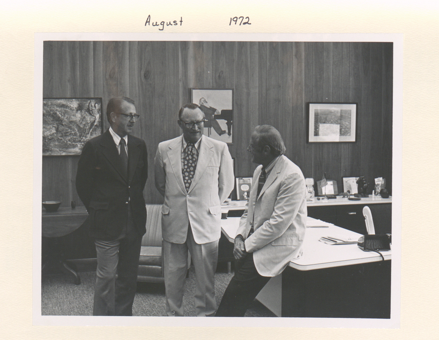 A black and white photograph of three individuals in a meeting.