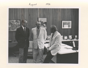 A black and white photograph of three individuals in a meeting.